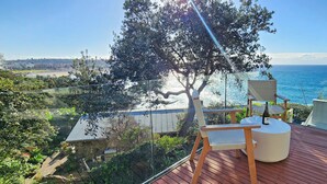A wooden deck with a chair and table, overlooking a beach and ocean. - Beachside living at its best! Bondi Beach Apartment. (Bondi Beach)