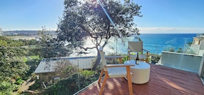 Un terrazzo in legno con una sedia e un tavolo, vista sulla spiaggia e sull'oceano.