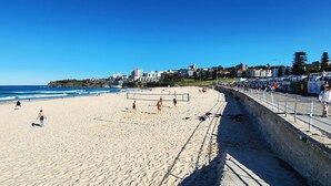 A beach with volleyball courts, a concrete barrier, and buildings in the background. - Beachside living at its best! Bondi Beach Apartment. (Bondi Beach)
