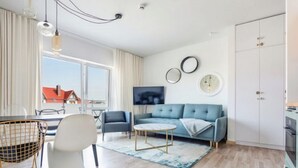 En moderne stue med en blå sofa, en hvid lænestol, et rundt sofabord og et spiseområde med bord og stole.