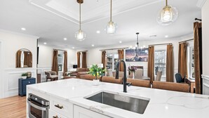Et moderne køkken med en central ø, rustfrie hårde hvidevarer og hængende lamper.