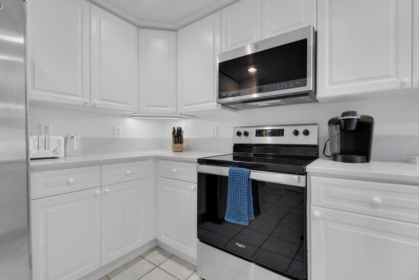 A modern kitchen with white cabinetry, a built-in microwave, a stove, and a coffee maker.