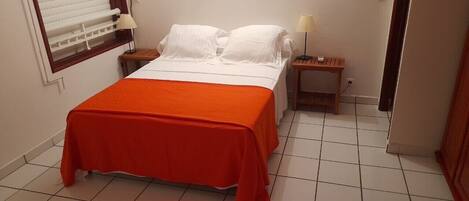 A hotel room with a bed, a nightstand, a lamp, and a window with blinds.