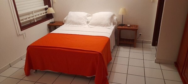 A hotel room with a bed, a nightstand, a lamp, and a window with blinds.