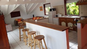 A kitchen with a central island, wooden stools, a refrigerator, and a window with a view of palm trees. - Top of Villa "La MARGUERITE (Deshaies)