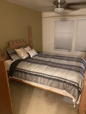 Un dormitorio con estructura de cama de madera, ventilador de techo y ventana con persianas.