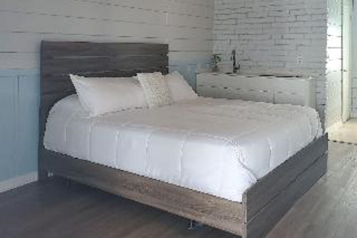 A bedroom with a wooden bed, white walls, and a brick wall.