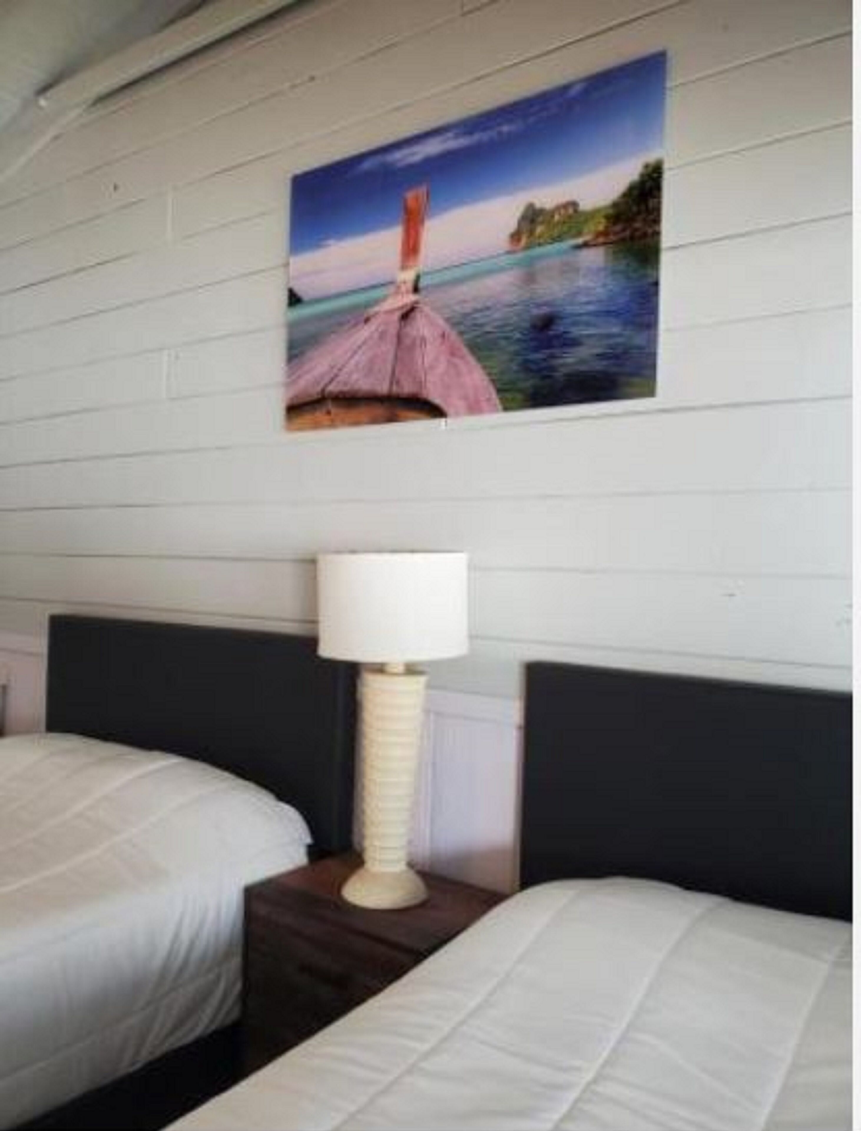 Et hotelværelse med to senge, et natbord med en lampe og et billed af et kystlandskab hængt på væggen.