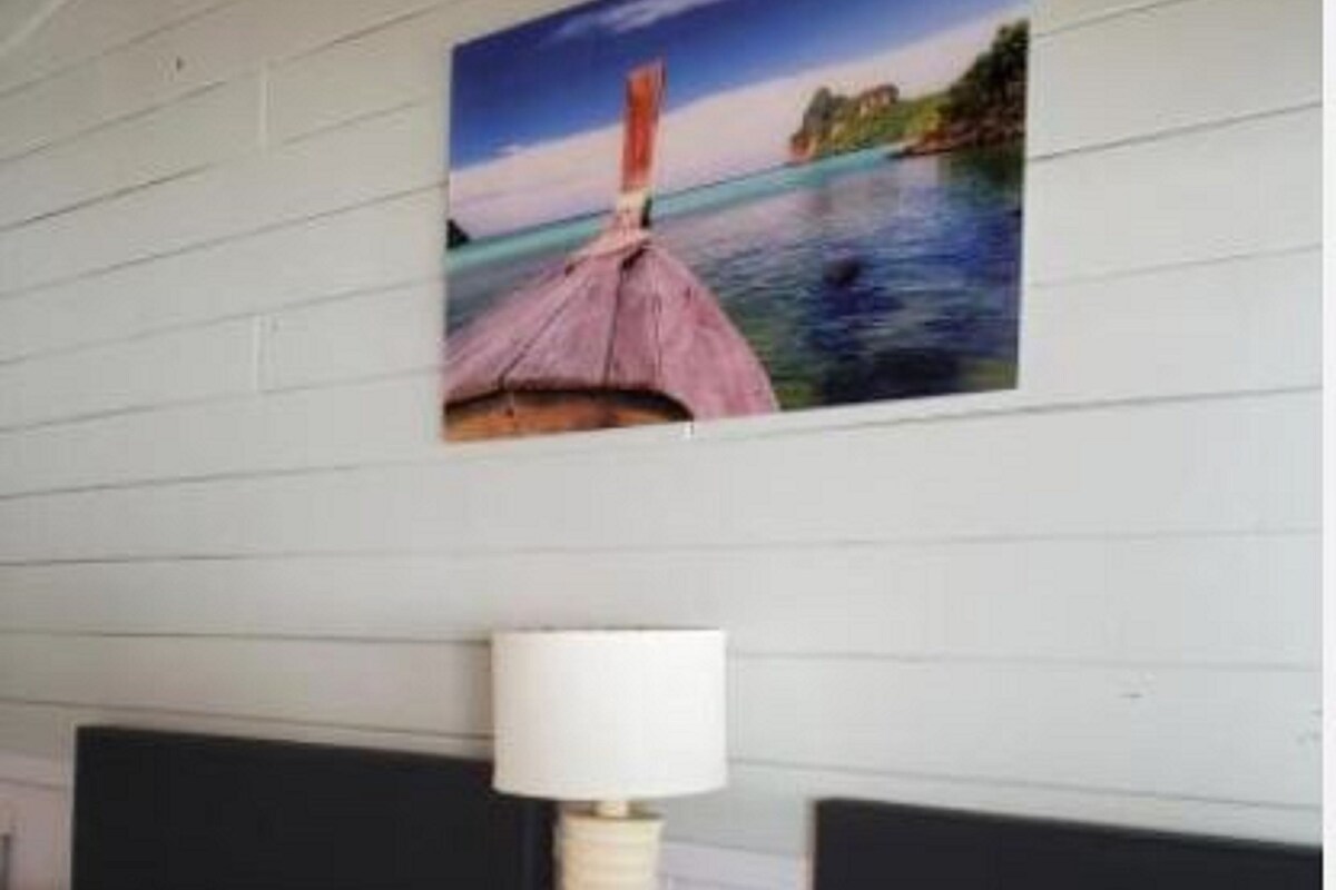 A hotel room with two beds, a nightstand with a lamp, and a wall-mounted picture of a coastal scene.