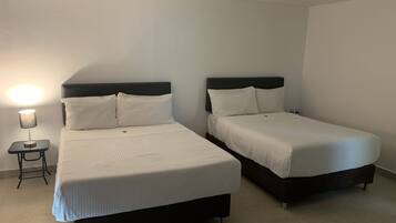 Two single beds with dark headboards and white bedding in a room with a small bedside table and lamp.