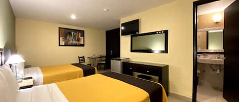 A hotel room with two beds, a desk, a chair, a TV, and a bathroom.