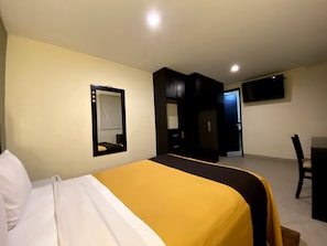 Een hotelkamer met een bed, een bureau, een stoel, een kledingkast en een televisie aan de muur.