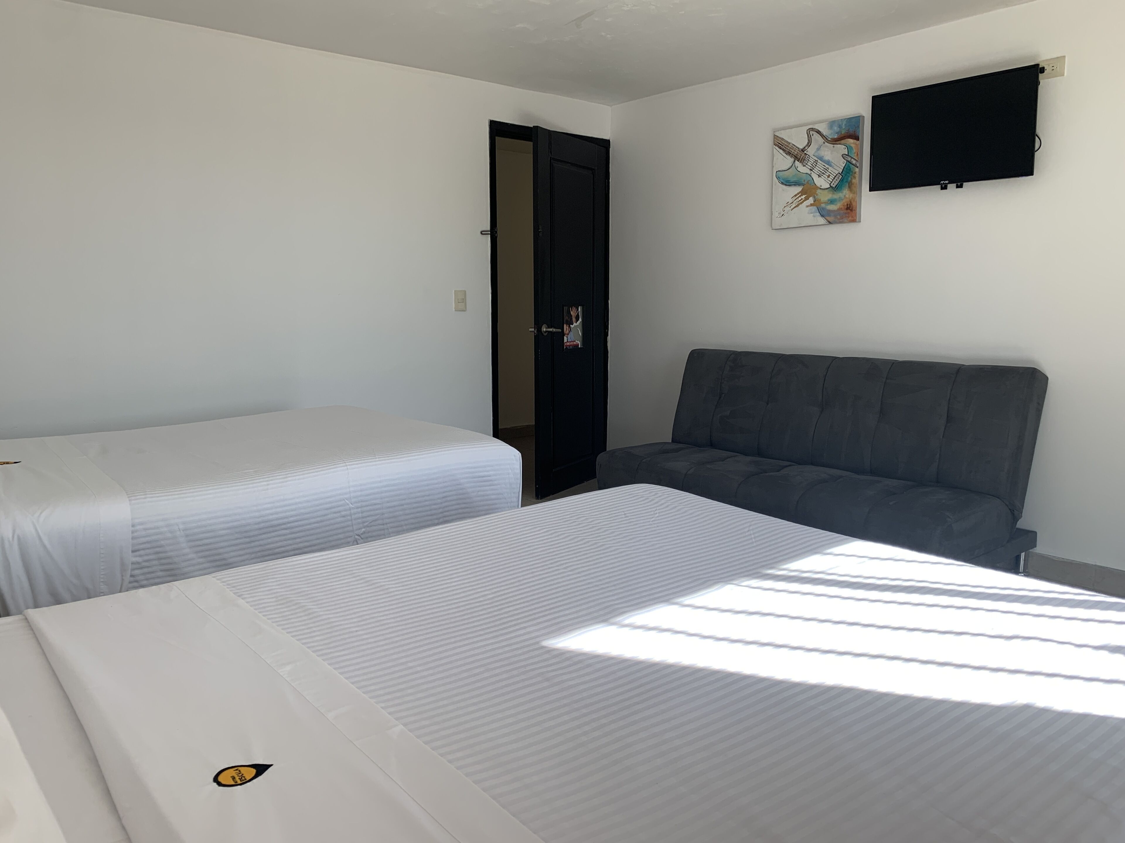 Ein Hotelzimmer mit zwei Einzelbetten, einem grauen Sofa, einem flachbildfernseher an der Wand und einer Tür zu einem weiteren Raum.