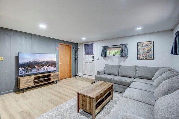 Un salon moderne avec un téléviseur à écran plat, un canapé gris, une table basse en bois et un tableau encadré au mur.