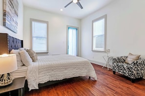 A bedroom with a bed, a nightstand, a lamp, a ceiling fan, a window, a door, and a patterned sofa. - Pet-Friendly Townhouse by St. Charles, Walk to street car (New Orleans)