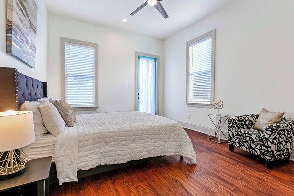 A bedroom with a bed, a nightstand, a lamp, a ceiling fan, a window, a door, and a patterned sofa. - Pet-Friendly Townhouse by St. Charles, Walk to street car (New Orleans)