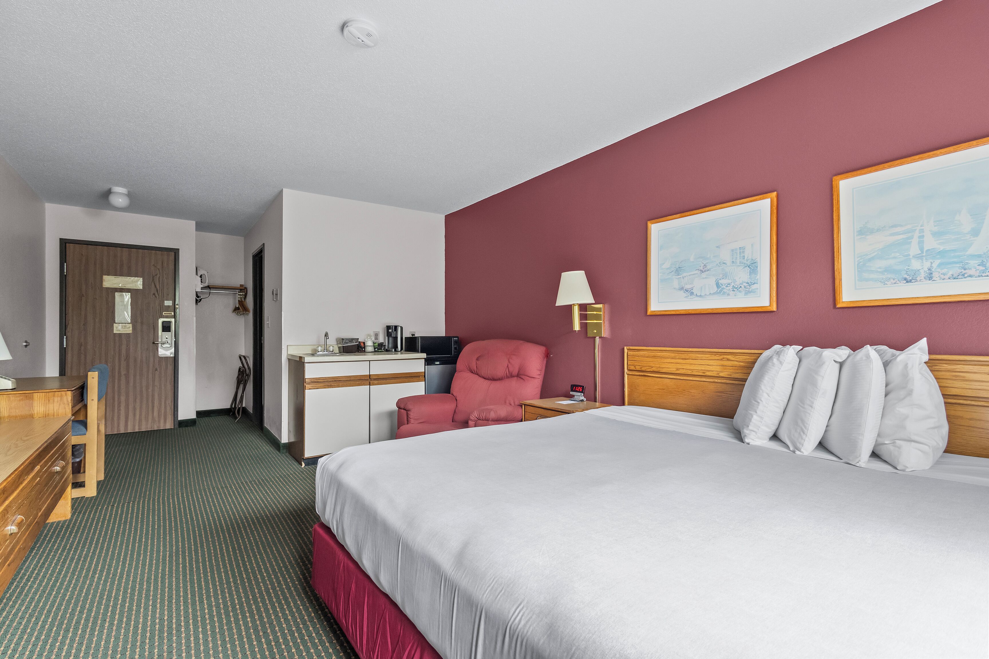A hotel room with a bed, a desk, a chair, a lamp, and two framed pictures on the wall.