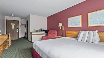 A hotel room with a bed, a desk, a chair, a lamp, and two framed pictures on the wall.