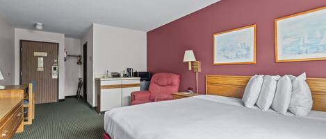 A hotel room with a bed, a desk, a chair, a lamp, and two framed pictures on the wall.