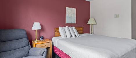 Een hotelkamer met een bed, een stoel, een nachtkastje en een lamp.