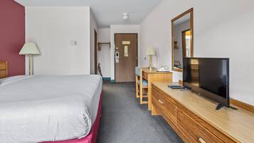 Hotellihuone, jossa on sänky, työpöytä, jossa on televisio, peili ja lamppu.