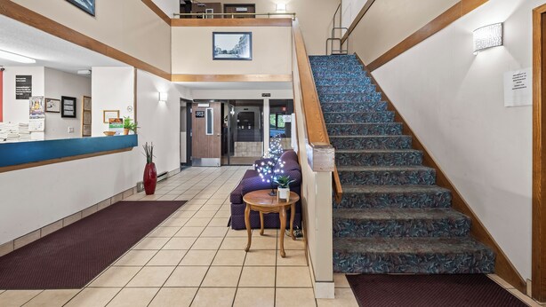 A hotel lobby with a reception desk, a staircase, and a seating area with a sofa and a small table. - Wautoma Inn by OYO Near Airport WI 73 (Wautoma)