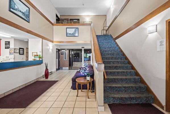 Un hall d’hôtel comprenant un comptoir d’accueil, un escalier et un espace détente avec un canapé et une petite table.