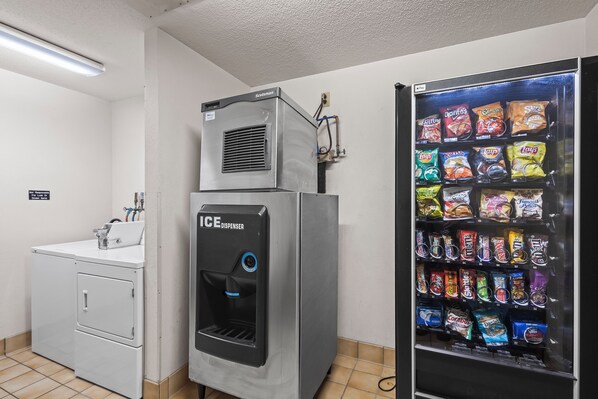 Un cuarto de lavandería con lavadora, dispensador de hielo y una máquina expendedora de aperitivos.
