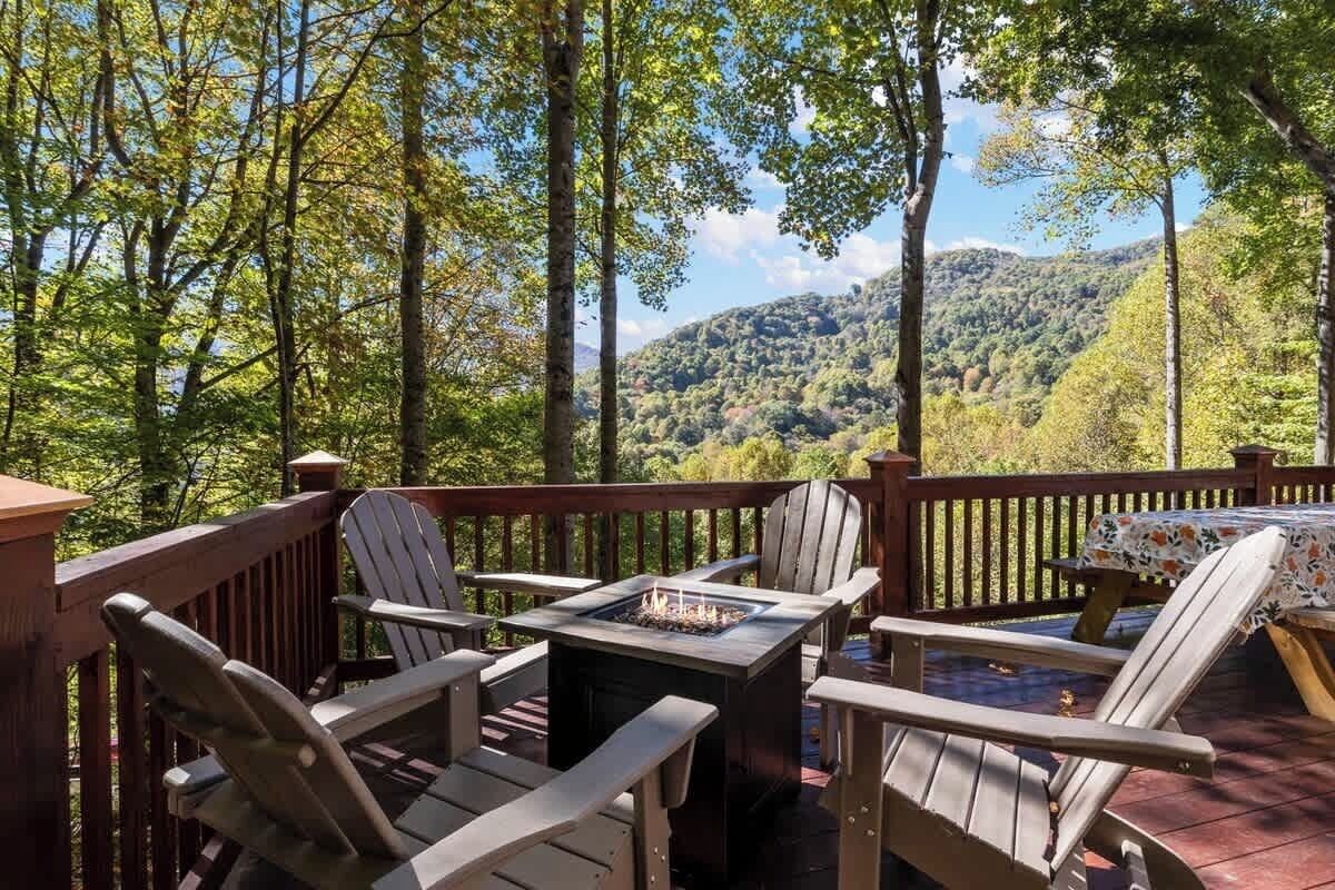 A deck with Adirondack chairs and a fire pit, overlooking a forested mountain.