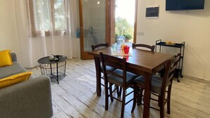 Un comedor con una mesa y sillas de madera, una mesita redonda con una silla, y un televisor montado en la pared.