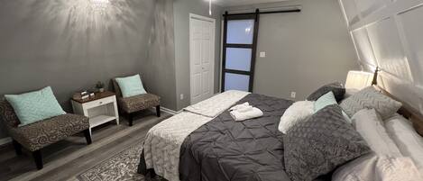 A bedroom with a bed, two chairs, a nightstand, a ceiling fan, and a window.