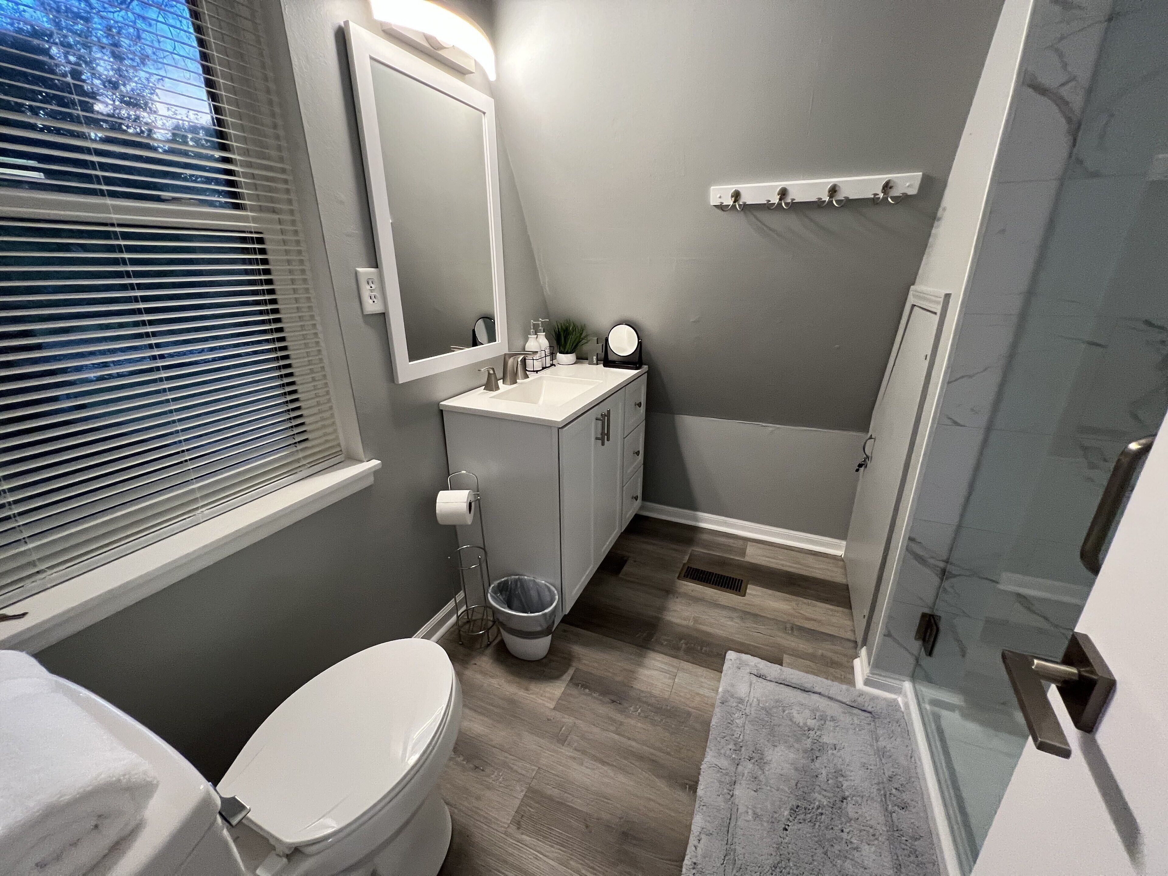 A bathroom with a toilet, sink, mirror, and shower.