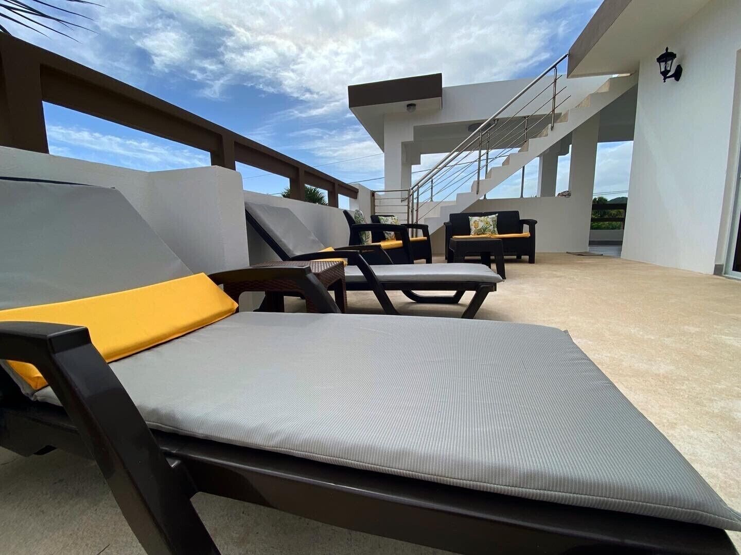 A modern outdoor lounge area with two lounge chairs and a sofa, featuring a concrete floor and a clear view of the sky.