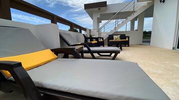 A modern outdoor lounge area with two lounge chairs and a sofa, featuring a concrete floor and a clear view of the sky.