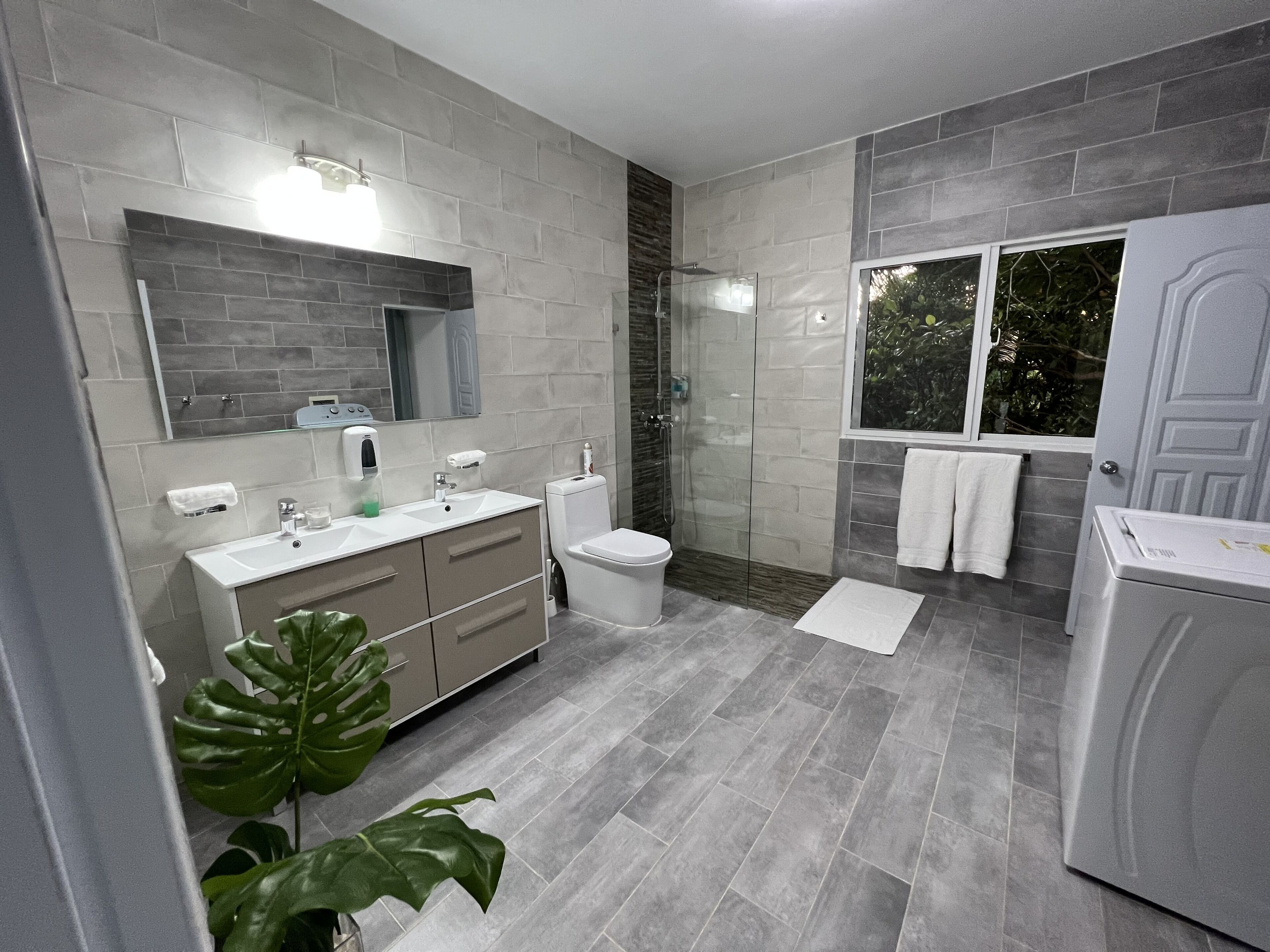A modern bathroom with a grey tile floor, a large mirror, a white sink, a toilet, and a shower area.