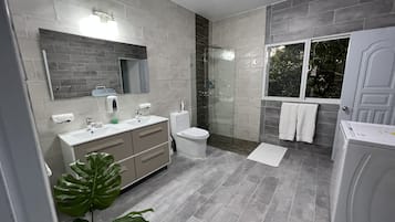 A modern bathroom with a grey tile floor, a large mirror, a white sink, a toilet, and a shower area.