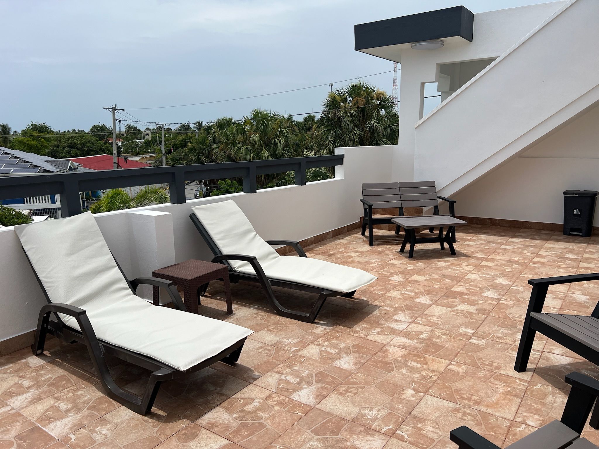 A rooftop terrace with two lounge chairs, a small table, and a bench.