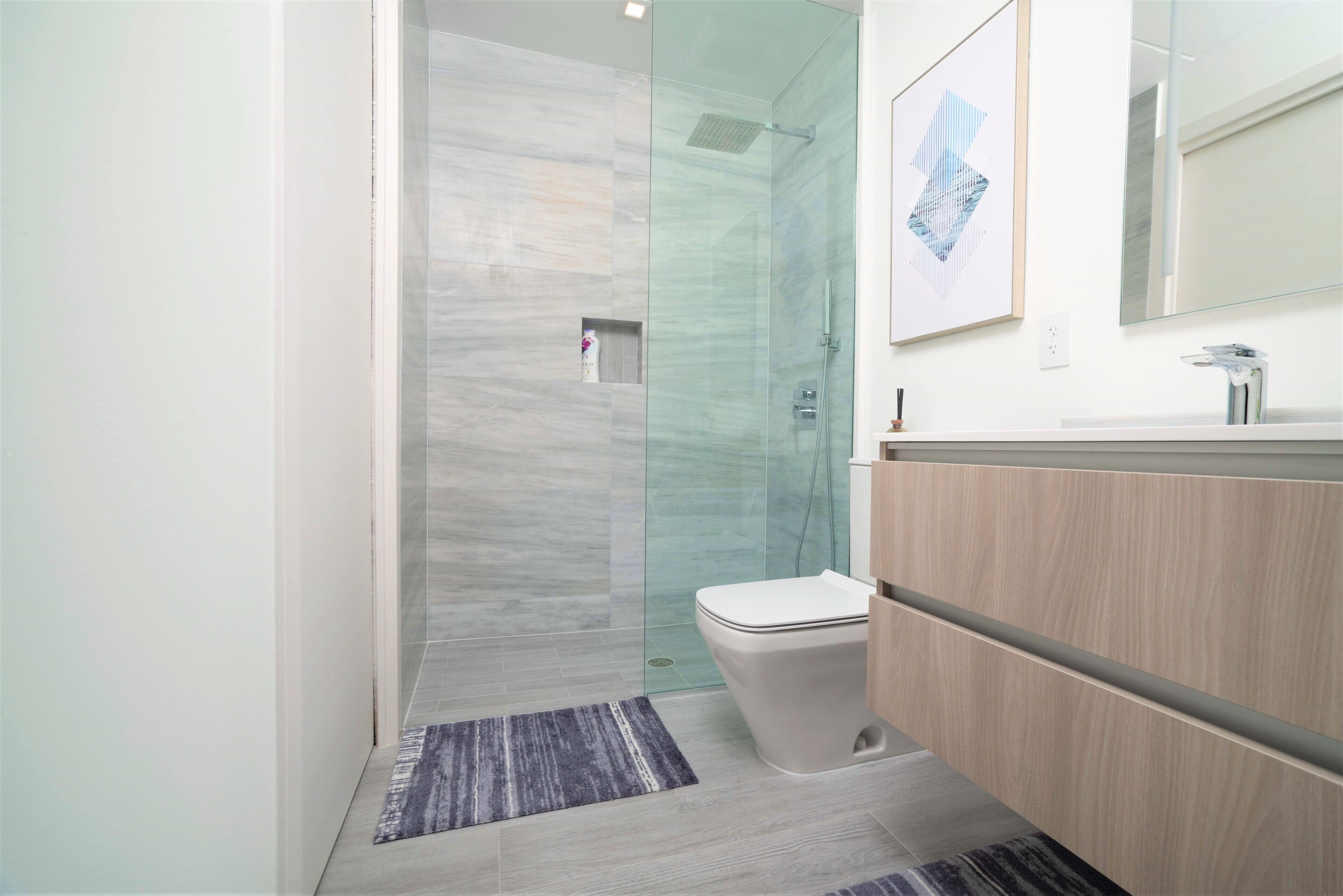 Un baño moderno con ducha de vidrio, inodoro y tocador de madera.