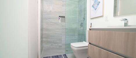 Un baño moderno con ducha de vidrio, inodoro y tocador de madera.