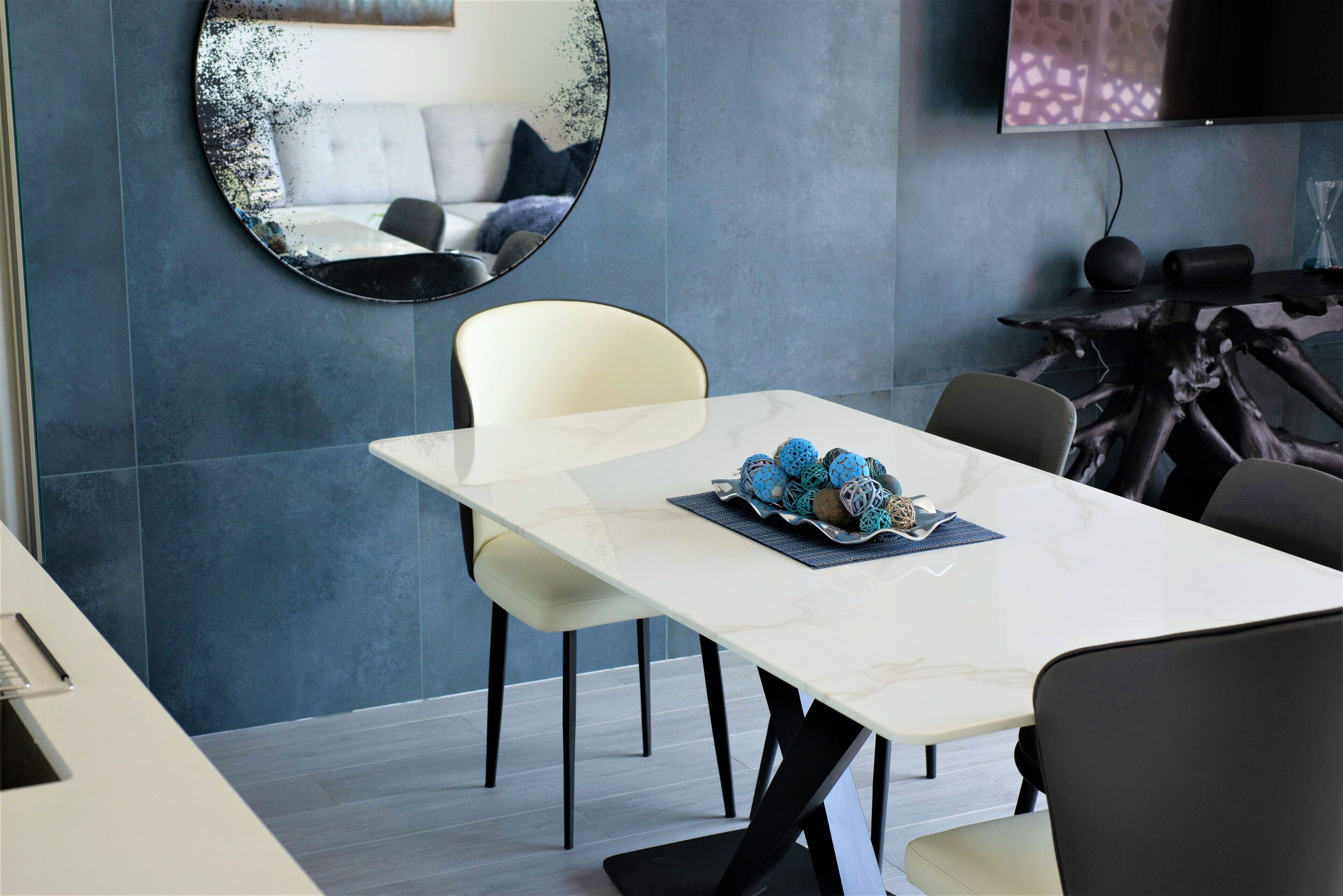 Un comedor moderno con una mesa de mármol blanco, sillas negras y un centro de mesa decorativo.
