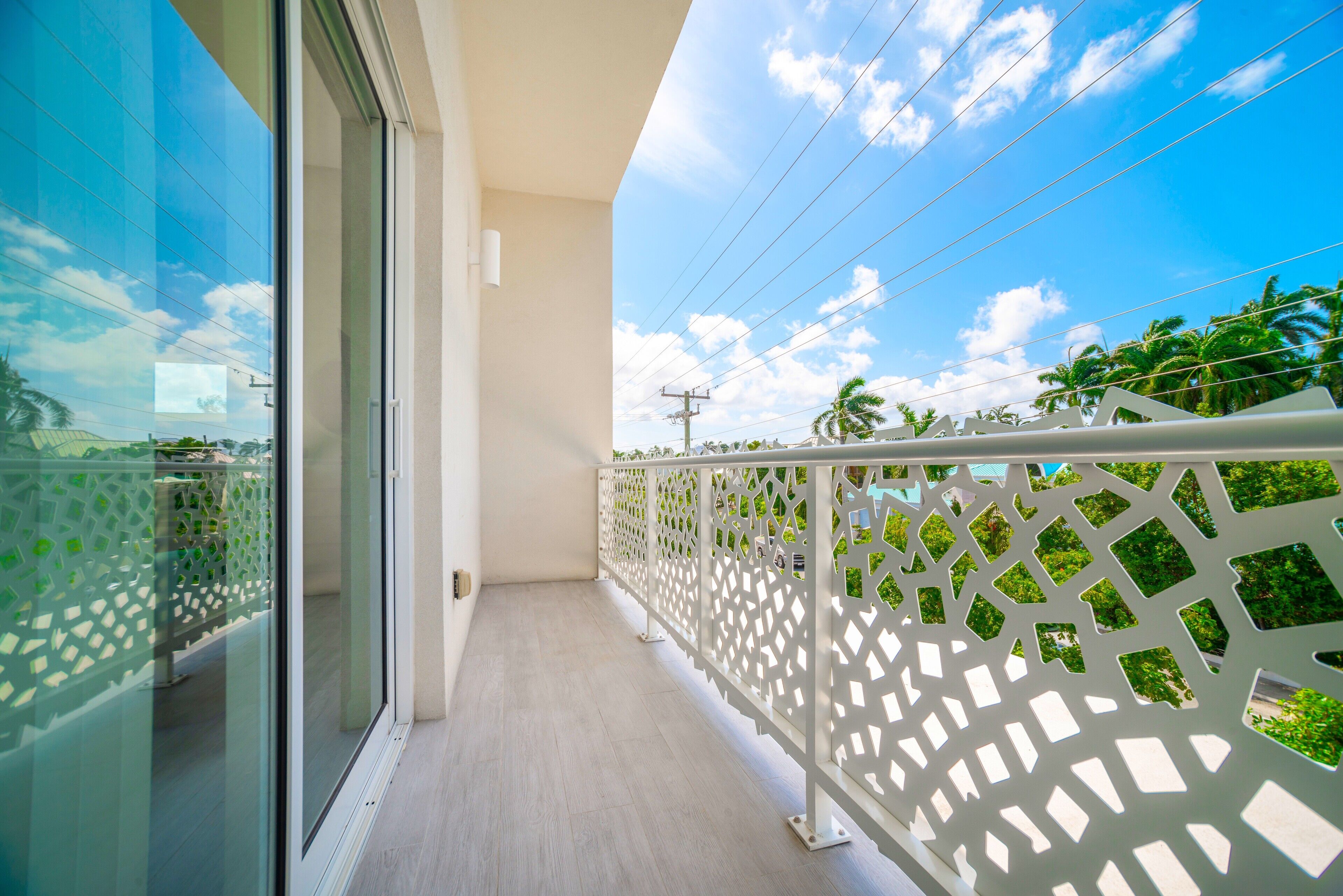 Un balcon doté d’une porte vitrée, d’une balustrade blanche et offrant une vue sur des palmiers et un ciel dégagé.
