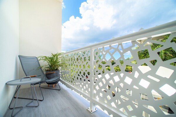 Un balcon avec une balustrade blanche à motifs, une chaise en métal gris, une petite table ronde et un pot de fleurs.