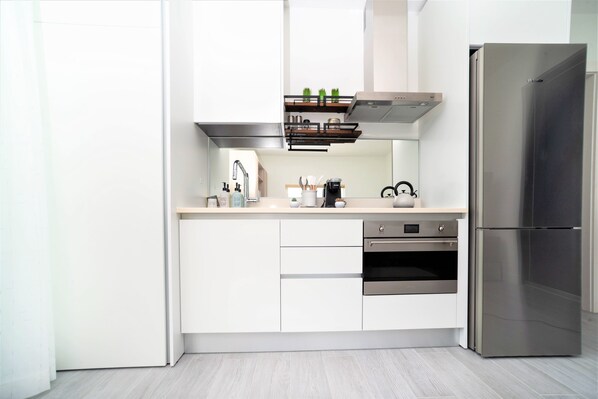 A modern kitchen with white cabinets, a stainless steel refrigerator, and a built-in oven. - Cayman Luxury Rentals at The Grove (Seven Mile Beach)