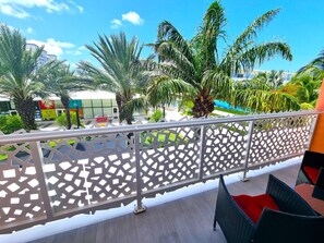 A balcony with a decorative metal fence, outdoor seating, and palm trees. - Cayman Luxury Rentals at The Grove (Seven Mile Beach)