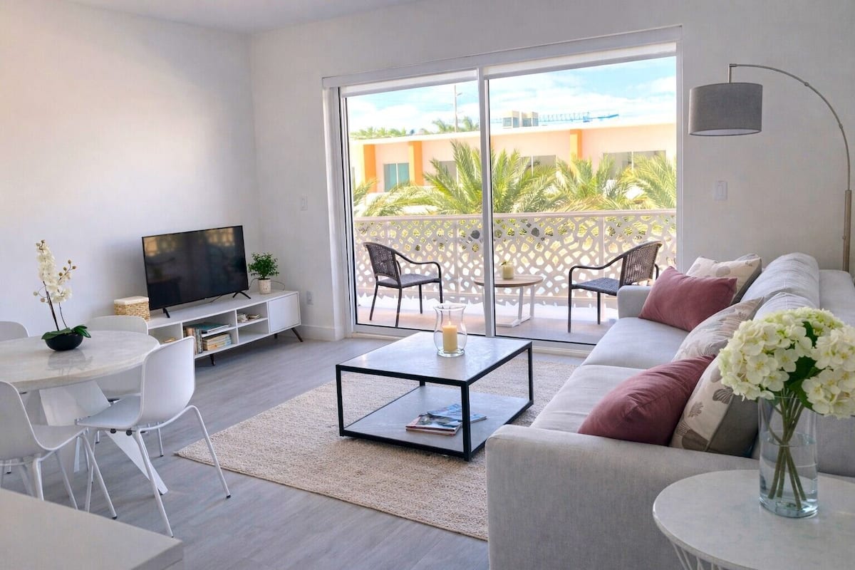 Una sala de estar moderna con un televisor de pantalla plana, una mesa de centro, un sofá y un comedor con sillas.