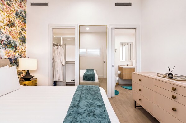 Een hotelkamer met een bed, een nachtkastje met een lamp, een dressoir, een badkamer met een spiegel en een kast met een badjas.