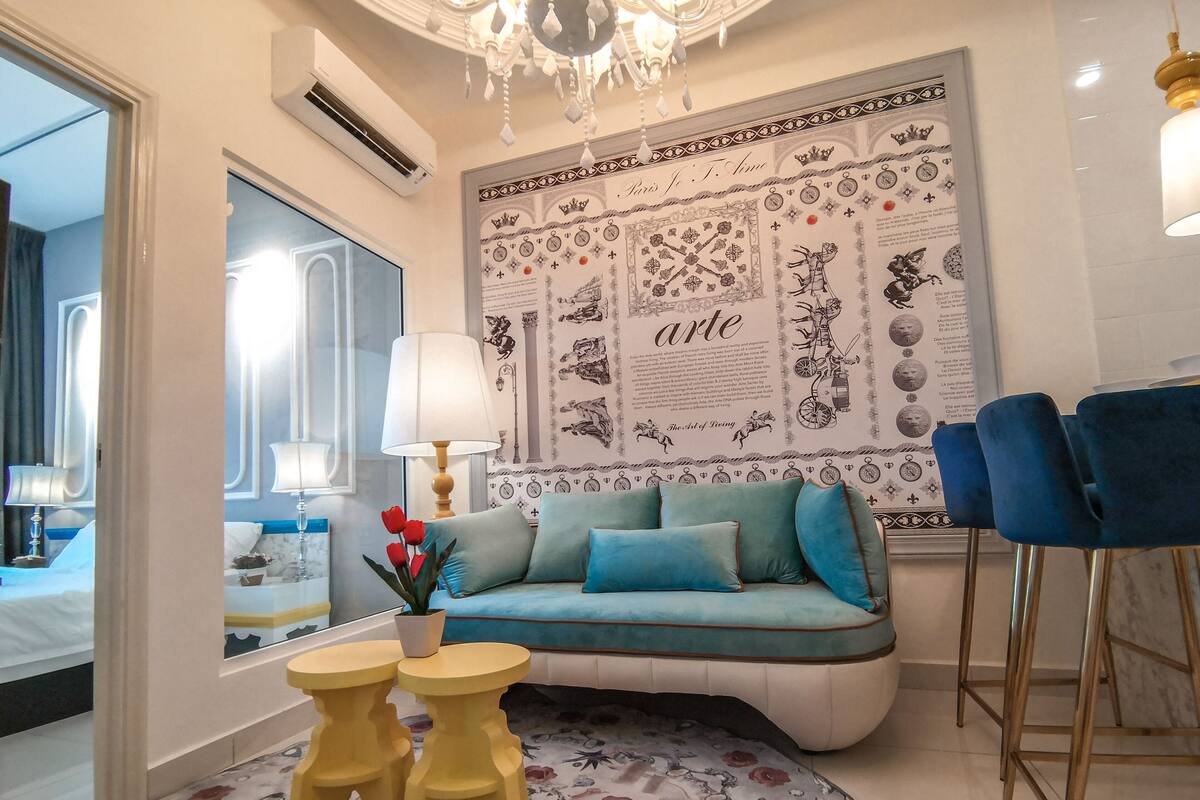 Una habitación de hotel moderna con un espejo grande, un sofá azul, una araña y un muro decorativo.