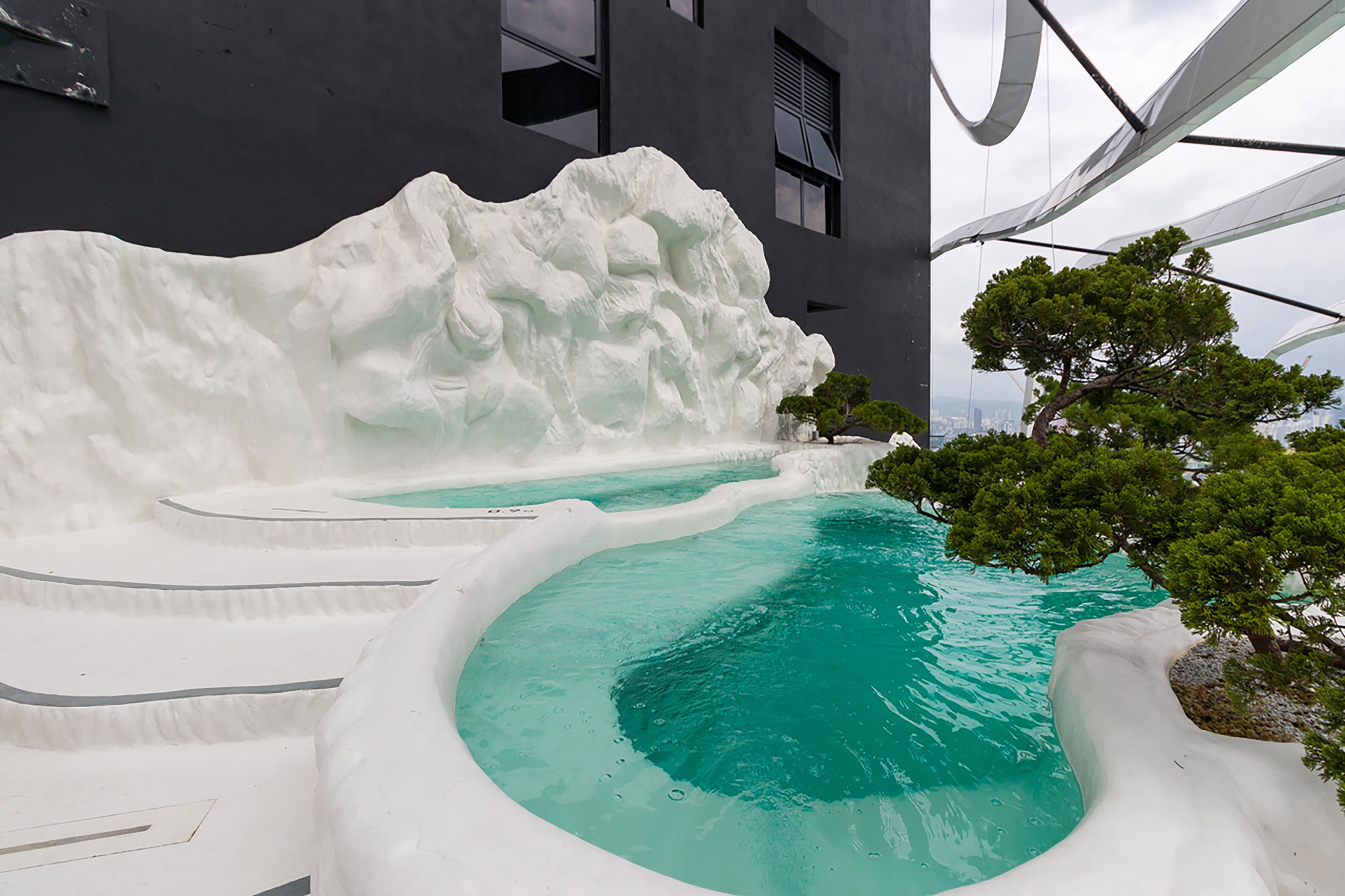 Un edificio moderno con piscina en la azotea, que presenta estructuras blancas con forma de olas y agua turquesa cristalina.