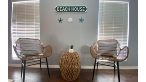 A room with two wicker chairs, a woven side table, and a wall sign reading "BEACH HOUSE" with star decorations. - Coco's Beach House Residential Home w/ POOL (Bradenton)