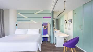 A modern hotel room with a large bed, a desk with a chair, a vanity, and a bathroom with a shower and toilet.